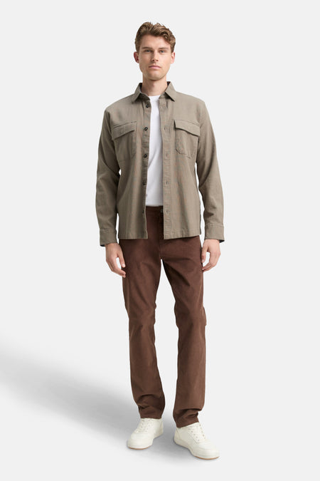 Pantalon coloré brun de Tom Tailor, en velours côtelé, porté avec une chemise ouverte et un t-shirt blanc uni.