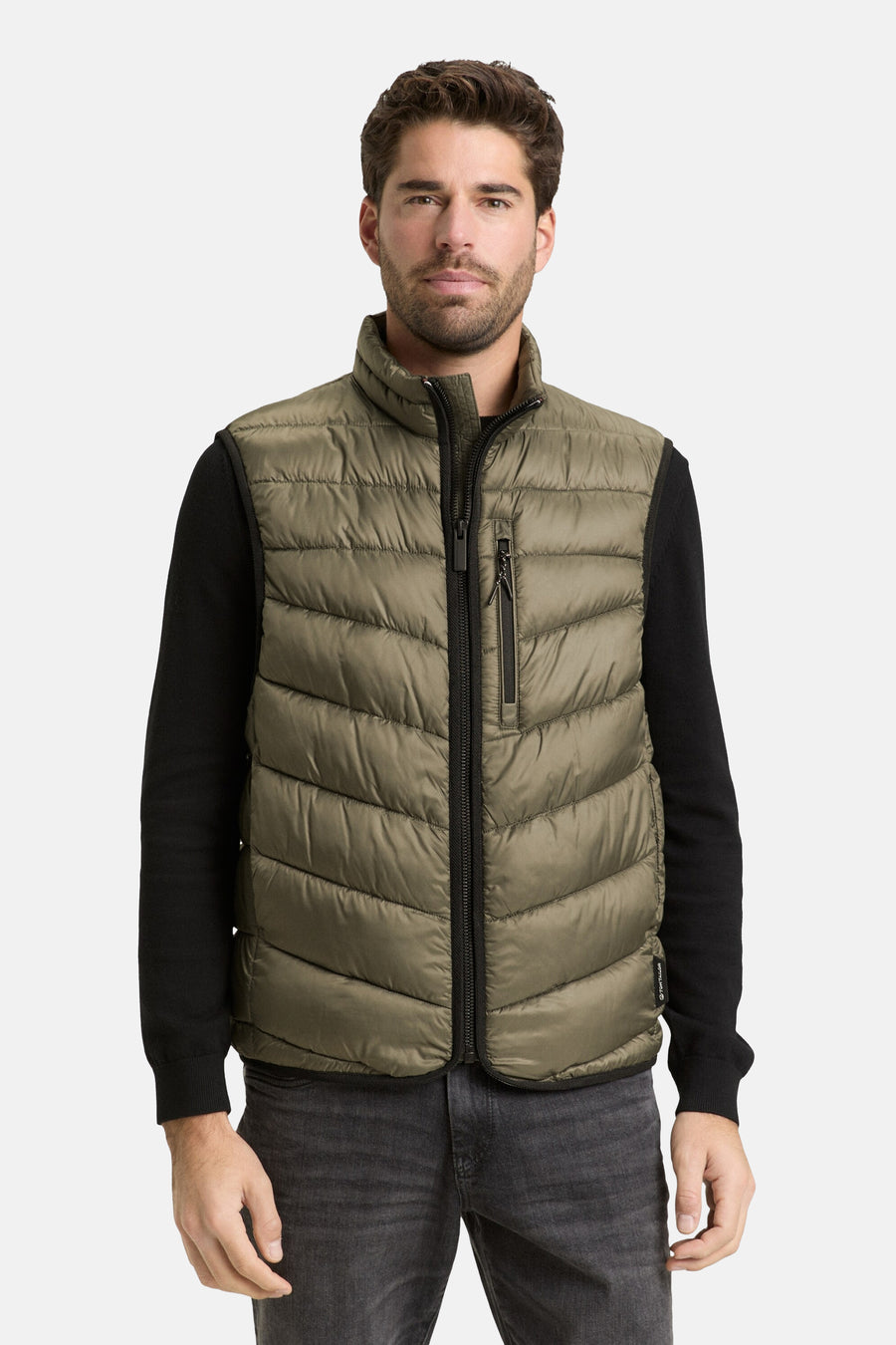 Veste sans manches kaki de Tom Tailor, avec fermeture éclair centrale, portée sur un pull noir et un jean gris délavé.