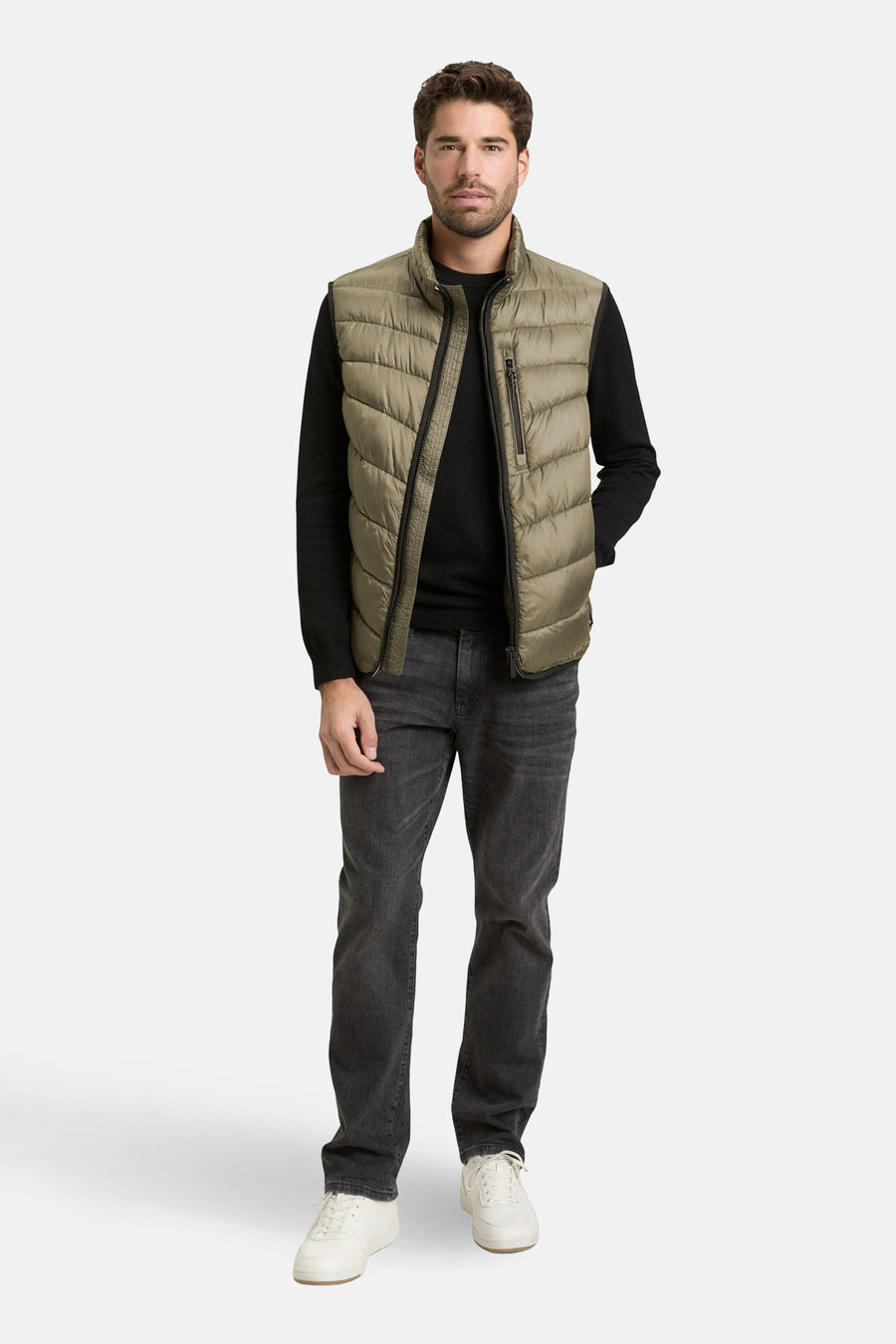 Veste sans manches kaki de Tom Tailor, portée sur un pull noir avec un pantalon en denim gris et des baskets blanches.