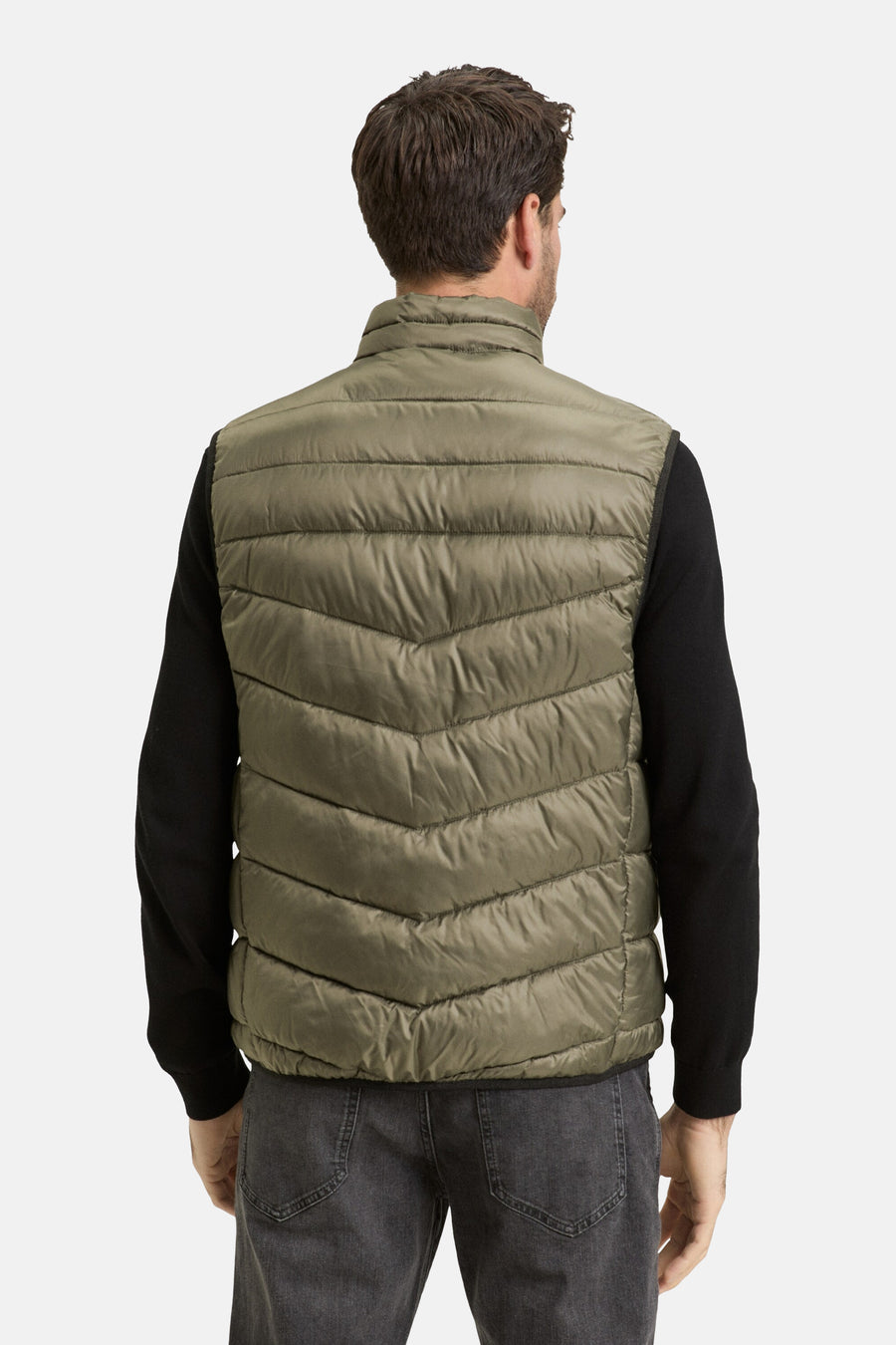 Veste sans manches kaki de Tom Tailor, modèle matelassé avec motif en chevrons, portée sur un pull noir et un jean gris, vue de dos.