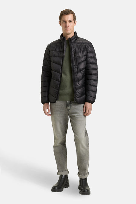 Veste de pluie noire par Tom Tailor, portée sur un pull vert et un jean gris délavé, avec des bottes noires.