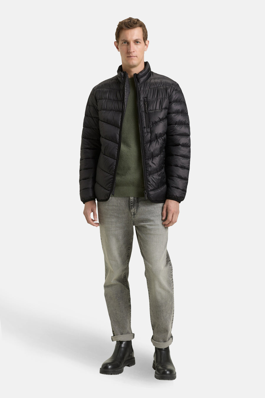 Veste de pluie noire par Tom Tailor, portée sur un pull vert et un jean gris délavé, avec des bottes noires.