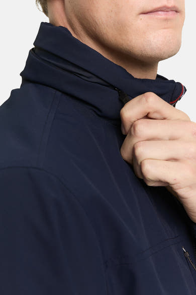 Veste courte bleue par Tom Tailor, col montant zippé et détail de la main ajustant le zip.