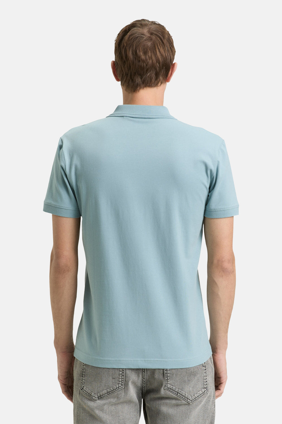 Polo bleu à manches courtes de Tom Tailor, vu de dos, porté avec un pantalon gris chiné.
