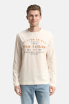 Witte T-shirt met lange mouwen van Tom Tailor, gedragen met een lichtblauwe jeans en witte sneakers.