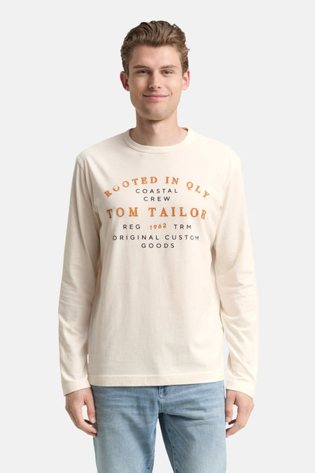 Witte T-shirt met lange mouwen van Tom Tailor, gedragen met een lichtblauwe jeans en witte sneakers.