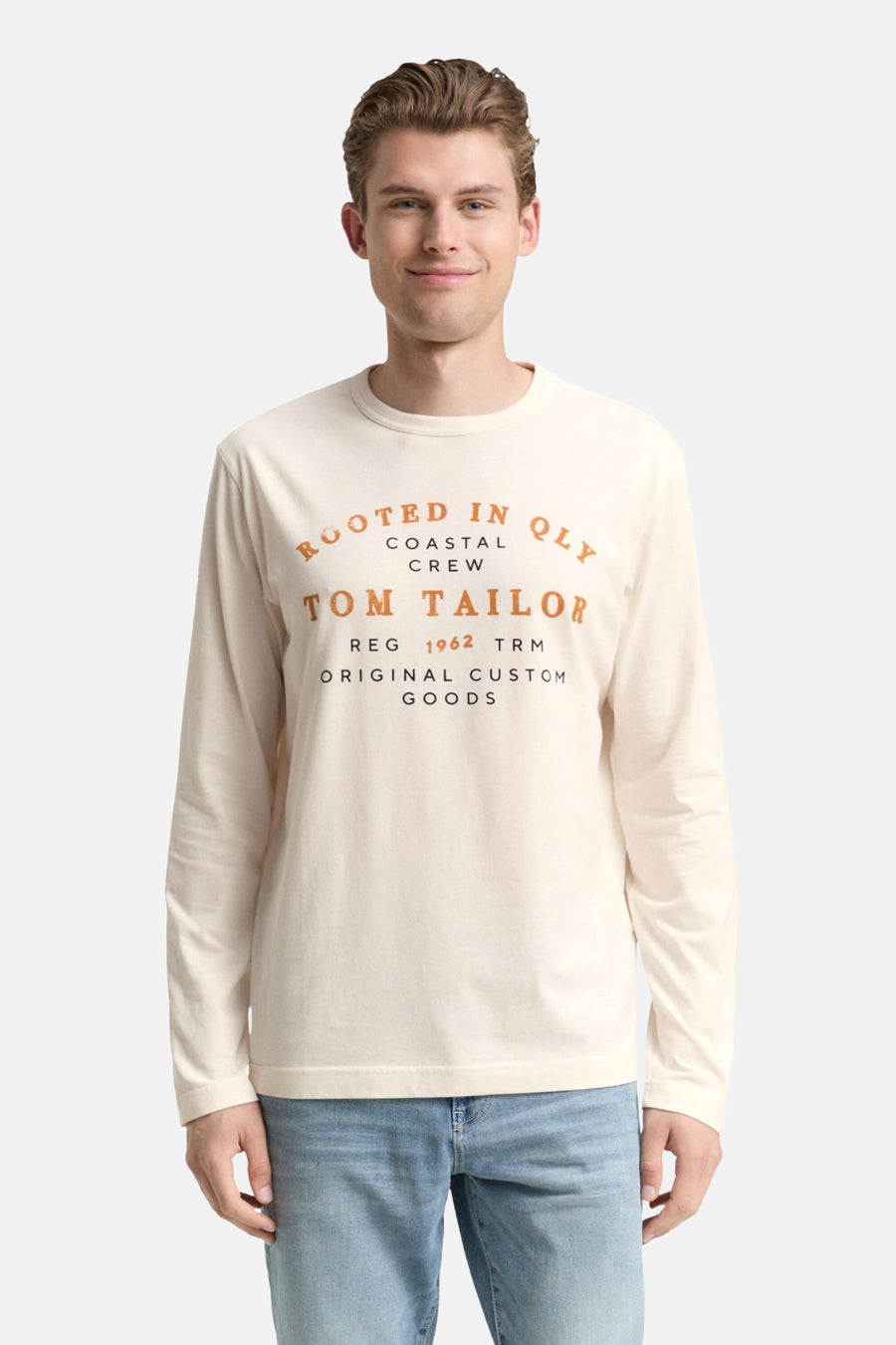 Witte T-shirt met lange mouwen van Tom Tailor, gedragen met een lichtblauwe jeans en witte sneakers.