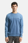 Blauwe sweater van Tom Tailor, gedragen met een donkergrijze jeans en witte sportschoenen.