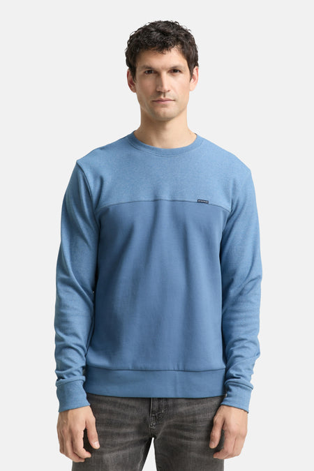 Sweat bleu de Tom Tailor avec un empiècement texturé et un pantalon gris foncé.