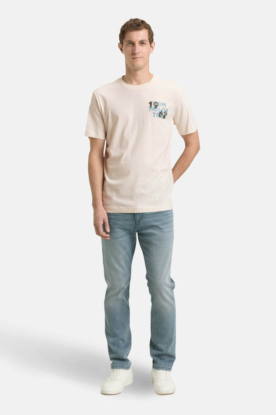 T-shirt à manches courtes écru de Tom Tailor, avec un logo décoratif sur la poitrine, porté avec un jean bleu et des baskets blanches.