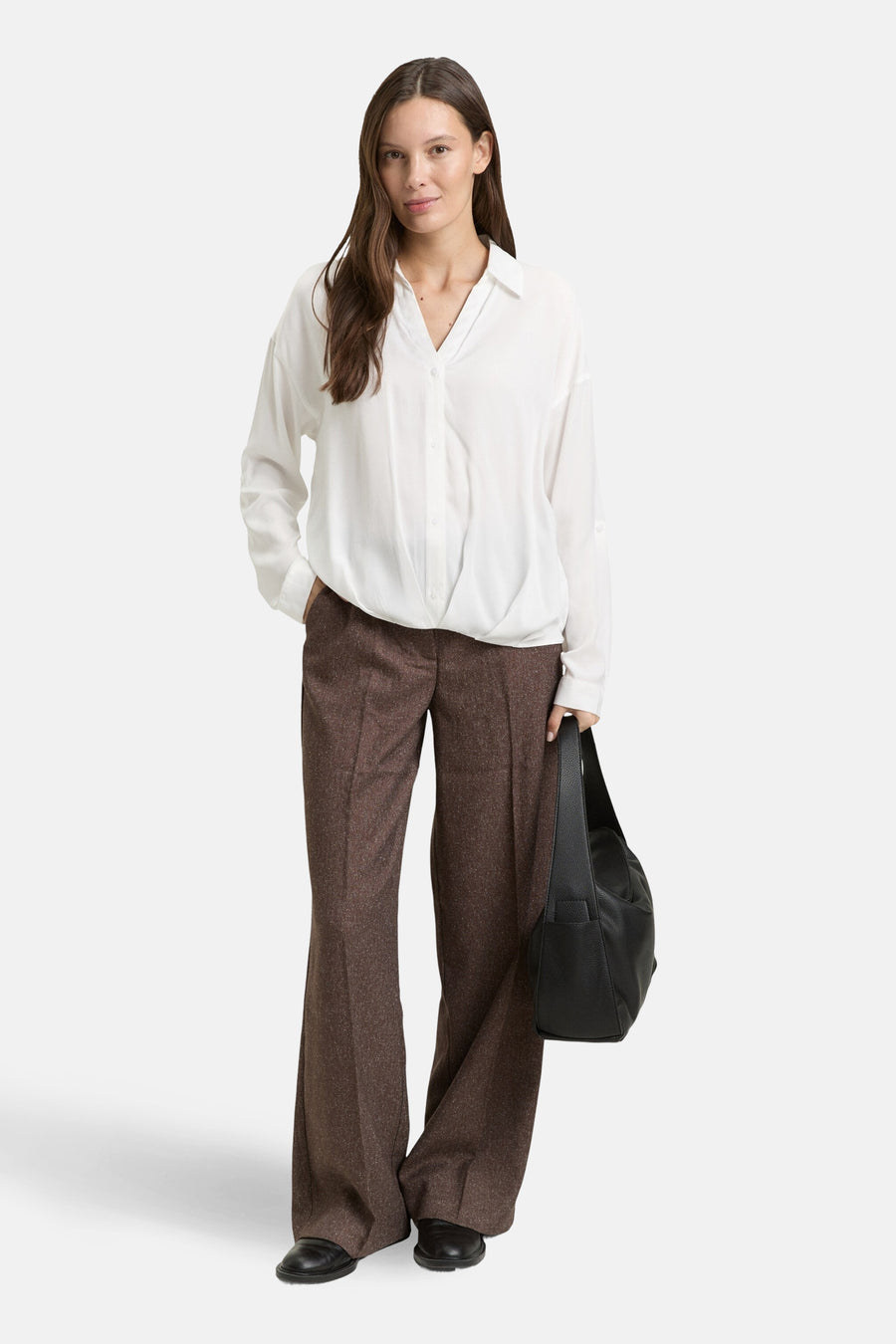 Chemisier blanc à manches longues de Tom Tailor, porté avec un pantalon marron à carreaux et un sac à main noir.