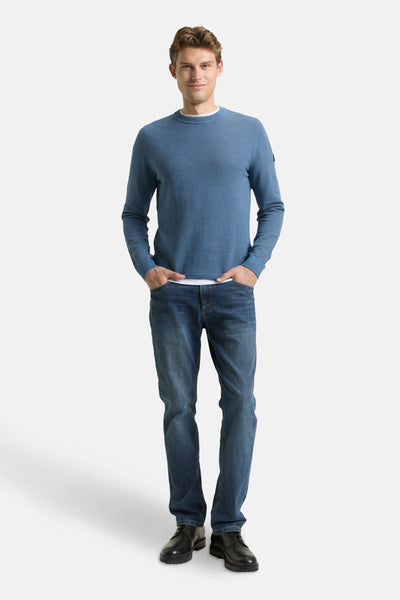 Pull à col rond bleu de Tom Tailor, porté avec un jean et des chaussures noires.