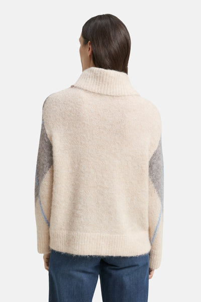 Pull à col roulé multicolore de Tom Tailor, avec motif losange sur les manches, porté avec un jean bleu.
