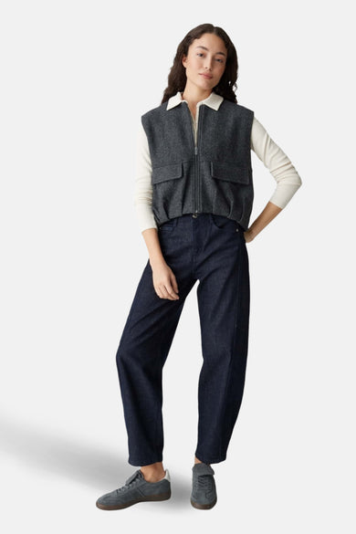Veste grise par OPUS avec fermeture éclair, portée sur un haut blanc et un jean bleu marine ample.