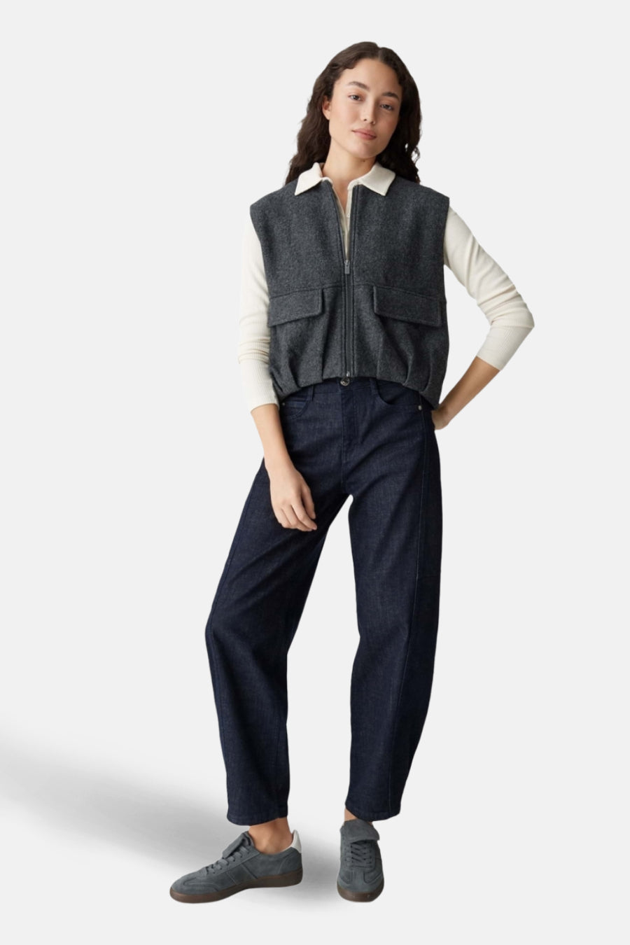 Veste grise par OPUS avec fermeture éclair, portée sur un haut blanc et un jean bleu marine ample.