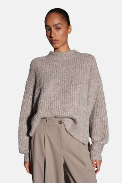 Pull à col rond taupe d'OPUS, en maille côtelée avec des détails pailletés discrets, porté avec un pantalon beige à plis.
