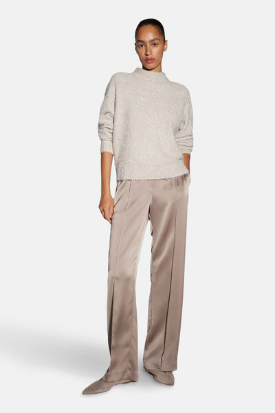 Pull col rond beige d'OPUS, porté avec un pantalon satiné et des chaussures plates.