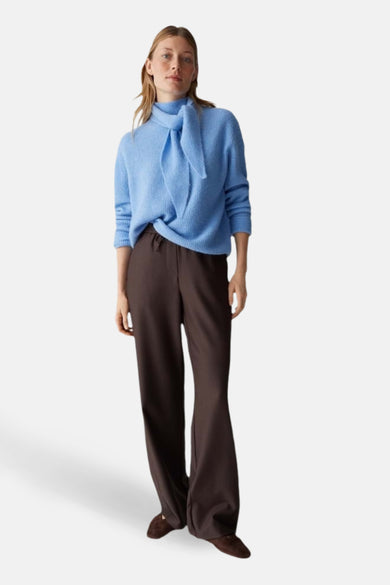 Pull bleu par OPUS avec un col noué, porté avec un pantalon marron ample.