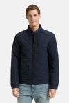 Korte blauwe jas van Tom Tailor met doorgestikt patroon, gedragen over een wit T-shirt en een casual spijkerbroek.