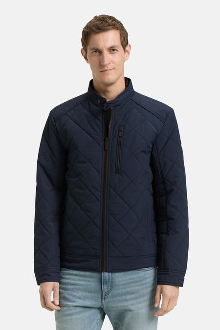 Korte blauwe jas van Tom Tailor met doorgestikt patroon, gedragen over een wit T-shirt en een casual spijkerbroek.