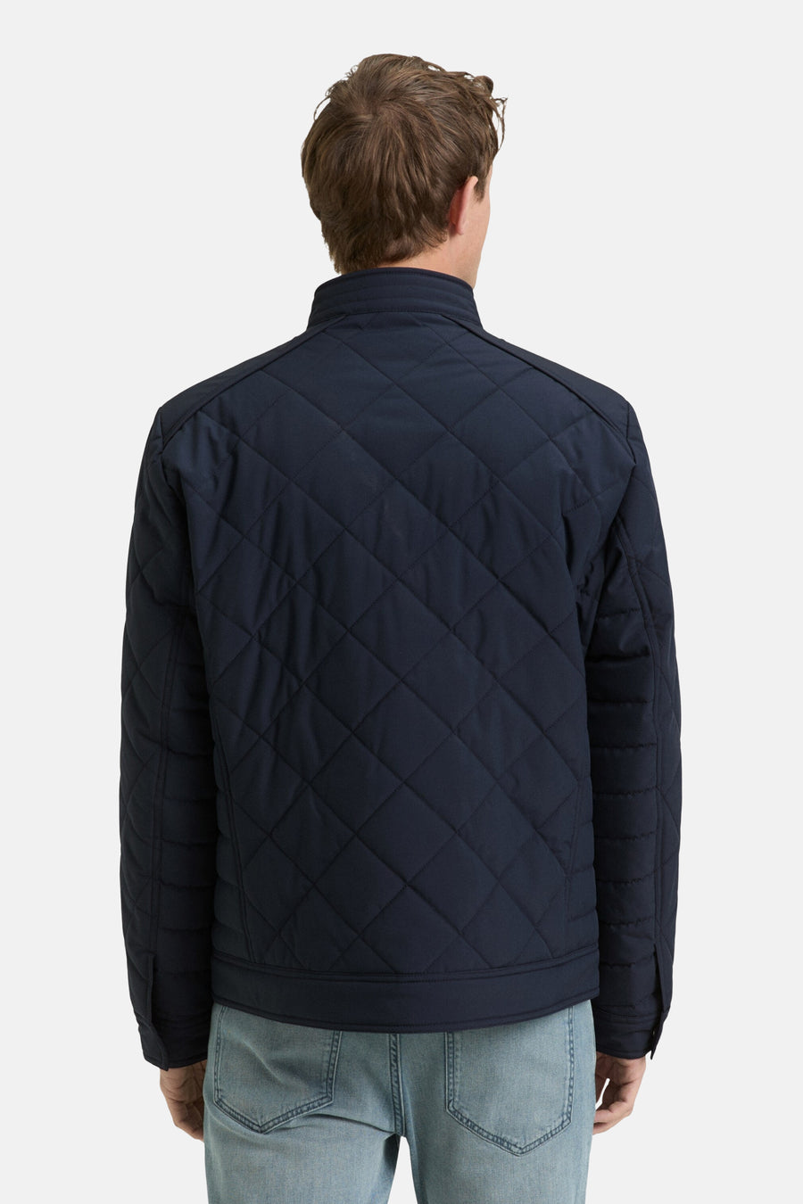Korte blauwe jas van Tom Tailor, gewatteerd met ruitpatroon, gedragen met een lichte spijkerbroek, van achteren gezien.