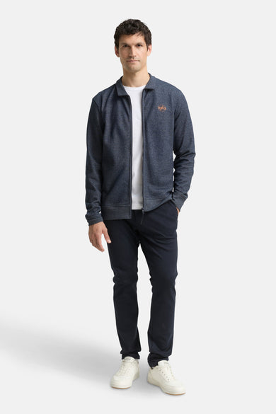 Gilet bleu de Tom Tailor, avec fermeture éclair et inscription « 1962 », porté sur un t-shirt blanc et un pantalon bleu marine.
