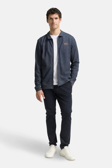 Gilet bleu de Tom Tailor, avec fermeture éclair et inscription « 1962 », porté sur un t-shirt blanc et un pantalon bleu marine.
