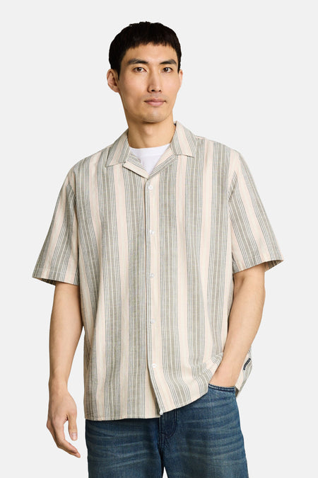 Chemise à manches courtes multicolore de Tom Tailor, rayée beige, grise et rose, portée ouverte sur un t-shirt blanc.