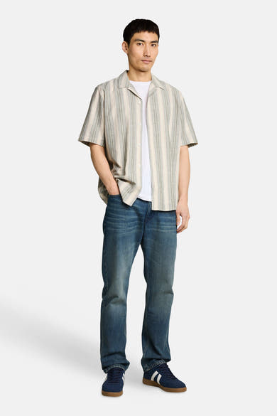 Chemise à manches courtes à rayures multicolores de Tom Tailor, ouverte sur un t-shirt blanc avec un jean et des baskets bleues.