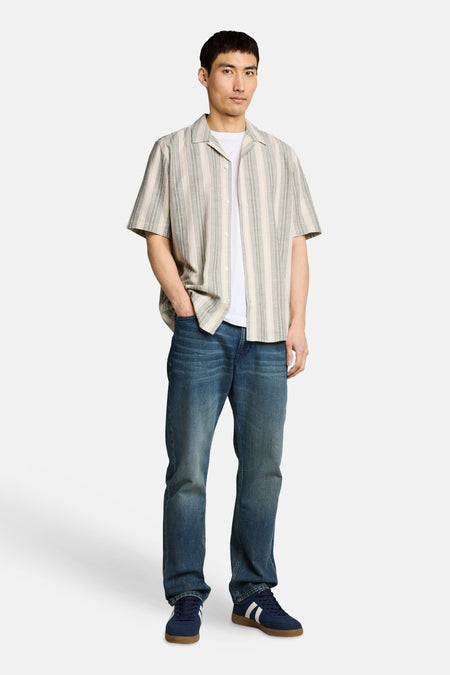 Chemise à manches courtes à rayures multicolores de Tom Tailor, ouverte sur un t-shirt blanc avec un jean et des baskets bleues.