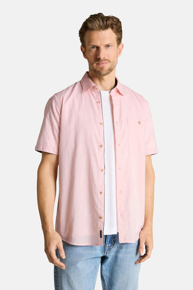 Chemise rose à manches courtes de Tom Tailor avec poche poitrine et liseré contrastant, portée ouverte sur un t-shirt blanc et un jean bleu.
