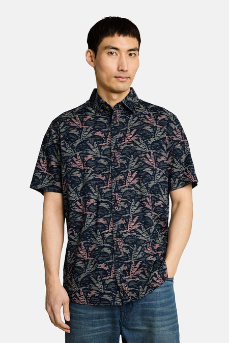 Chemise à manches courtes multicolore de Tom Tailor, motif feuilles rose et gris sur fond bleu marine, portée avec un jean.