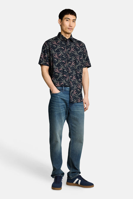 Chemise à manches courtes multicolore de Tom Tailor, à motifs feuilles roses et beiges, portée avec un jean et des baskets bleues.