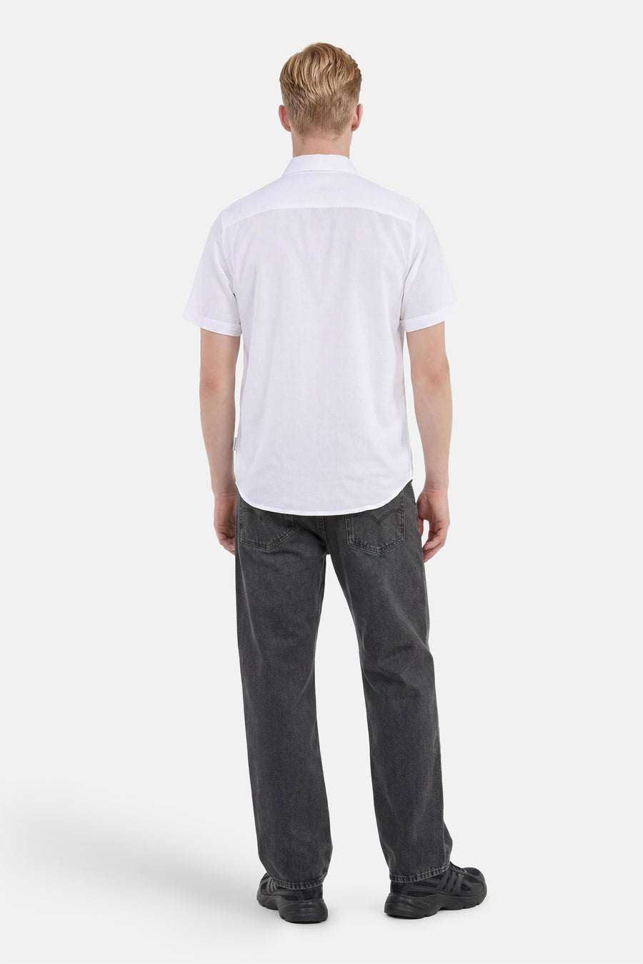 Chemise à manches courtes blanche de Tom Tailor, vue de dos sur un homme portant un jean gris foncé et des baskets noires.