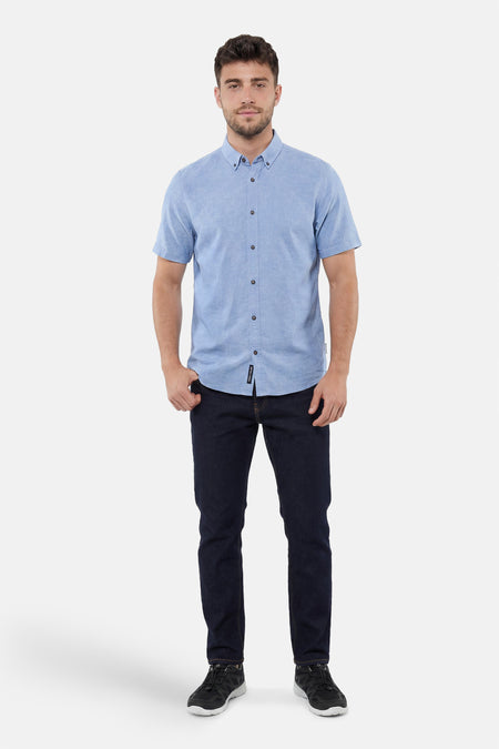 Chemise bleue chinée à manches courtes de Tom Tailor, boutonnée, avec un jean foncé et des baskets noires.