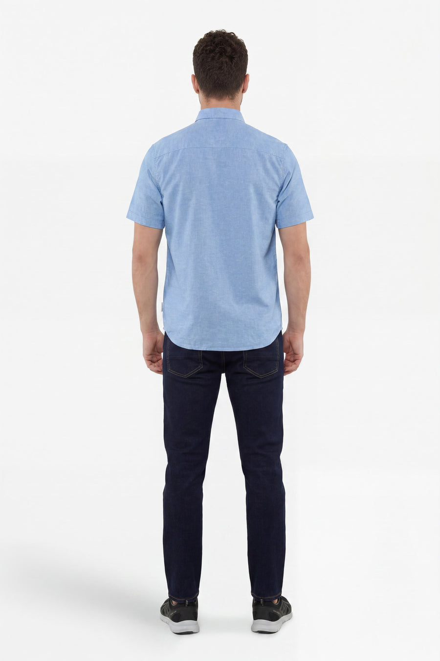 Blauw overhemd met korte mouwen van Tom Tailor, van achteren gedragen door een man in donkere jeans en sneakers.