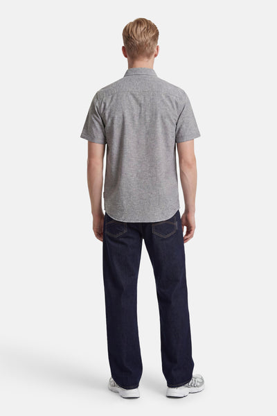 Chemise à manches courtes grise de Tom Tailor portée par un homme vu de dos avec un jean foncé et des baskets.