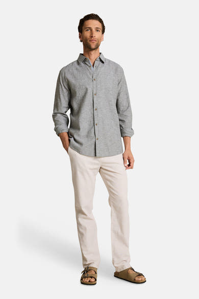 Chemise à manches longues verte par Tom Tailor, boutonnée, portée avec un pantalon clair et des sandales.