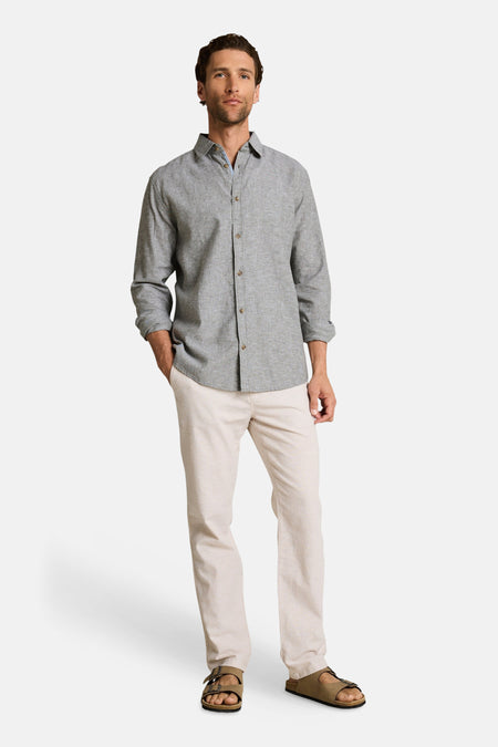 Chemise à manches longues verte par Tom Tailor, boutonnée, portée avec un pantalon clair et des sandales.