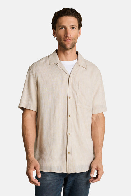 Chemise à manches courtes beige de Tom Tailor, à fines rayures verticales, col cubain, portée ouverte sur un t-shirt blanc.