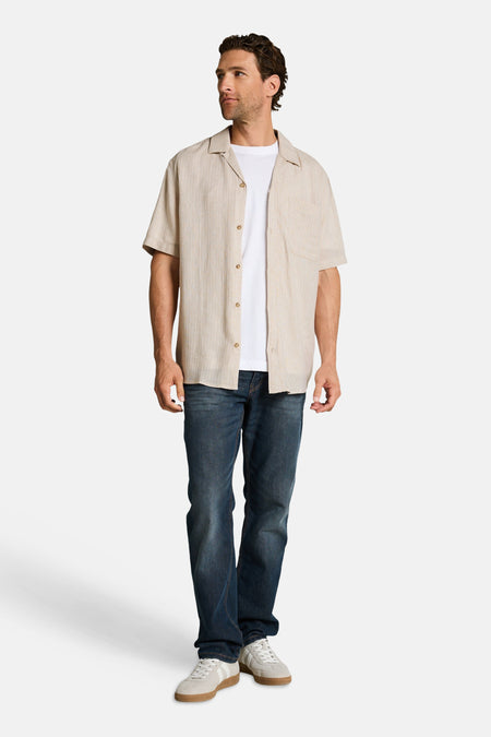 Chemise à manches courtes beige de Tom Tailor à fines rayures verticales, portée sur un t-shirt blanc et un jean.