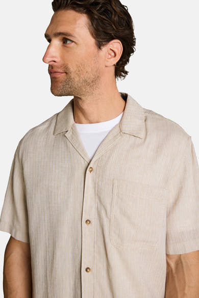 Beige korte mouwen overhemd van Tom Tailor met fijne verticale strepen, cubaanse kraag en borstzak, gedragen open over een wit T-shirt.