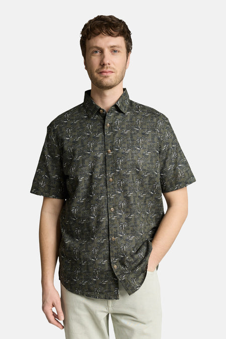 Chemise à manches courtes verte de Tom Tailor à motif feuillage blanc et gris, portée par un homme avec un pantalon clair.