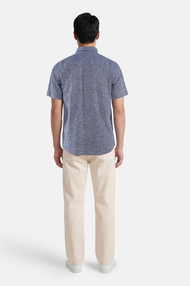 Blauw overhemd met korte mouwen van Tom Tailor, met subtiel stippenpatroon, van achteren gezien, gedragen met een beige broek en witte sneakers.