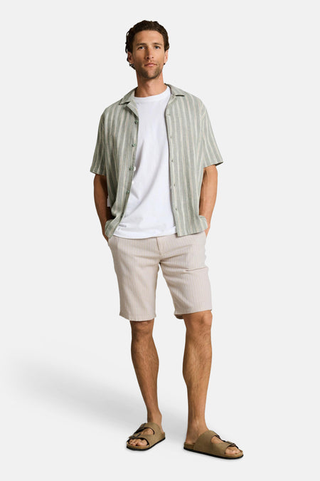 Bermuda beige de Tom Tailor avec rayures verticales, porté avec un t-shirt blanc et des sandales marron.