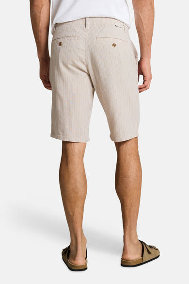 Bermuda beige de Tom Tailor, à rayures verticales fines, porté avec un t-shirt blanc et des sandales marron, vue de dos.
