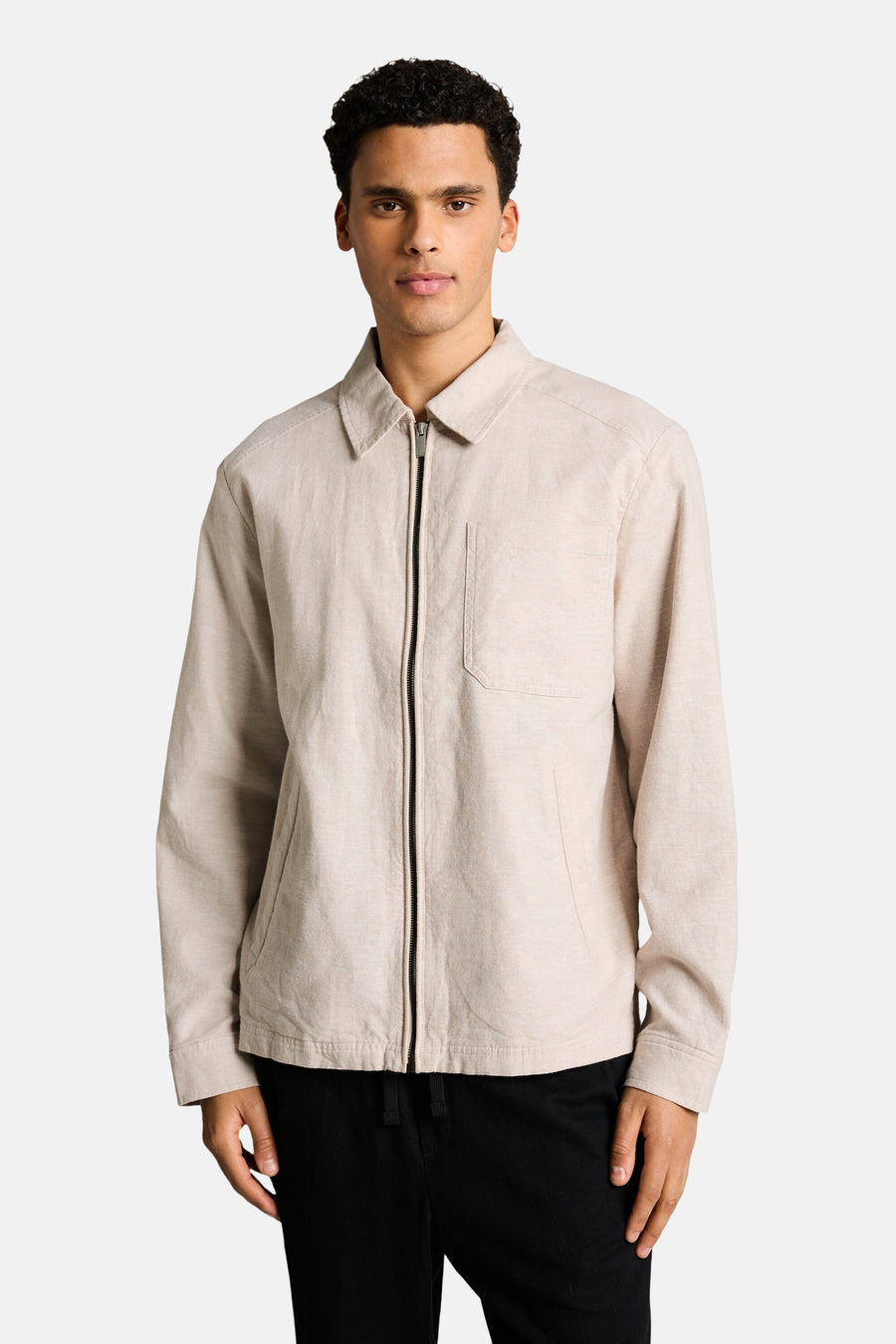 Veste beige de Tom Tailor, avec fermeture éclair et poche de poitrine, portée sur un pantalon noir.
