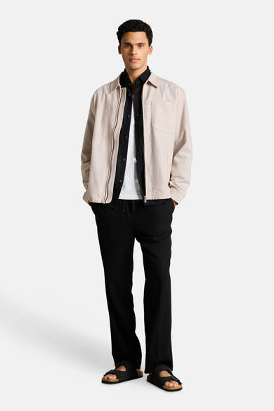 Veste beige de Tom Tailor, portée avec chemise noire, t-shirt blanc, pantalon noir et sandales.