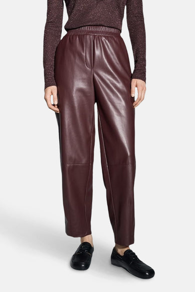 Pantalon bordeaux en similicuir par OPUS, avec une taille élastique et des chaussures noires plates.
