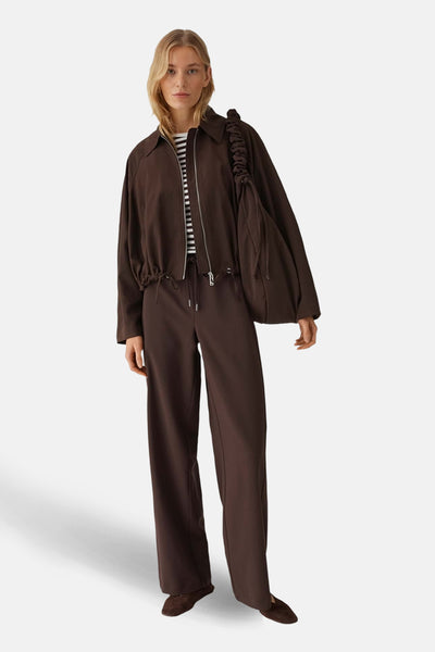Pantalon de costume brun de OPUS, coupe droite ample avec cordon de serrage, porté avec un t-shirt rayé et une veste marron.